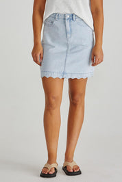 A model wearing the Vale Scalloped Denim Skirt in colour Bleach (Blue), from the front, cropped image