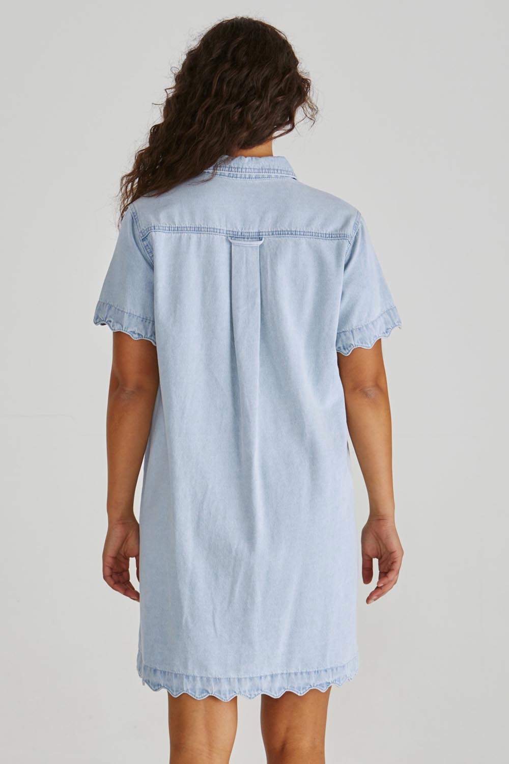 A model wearing the Vale Scalloped Denim Dress in colour Bleach (Blue), from the back