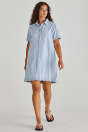 A model wearing the Vale Scalloped Denim Dress in colour Bleach (Blue), from the front, showing the whole outfit