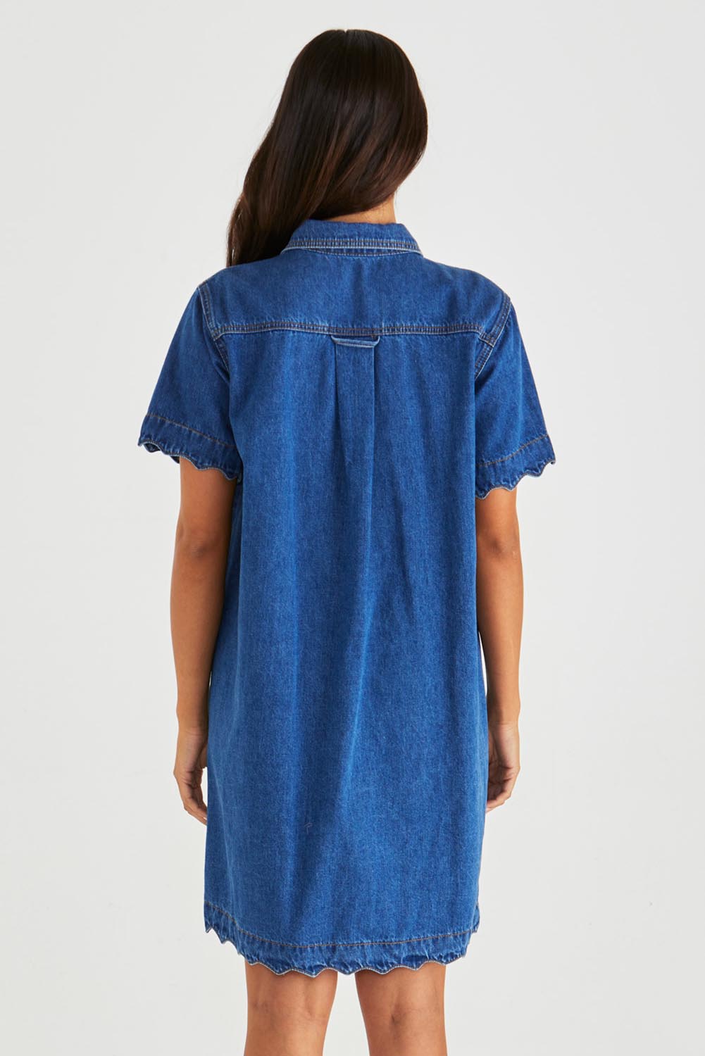 A model wearing the Vale Scalloped Denim Dress in colour Midblue (Blue), from the back