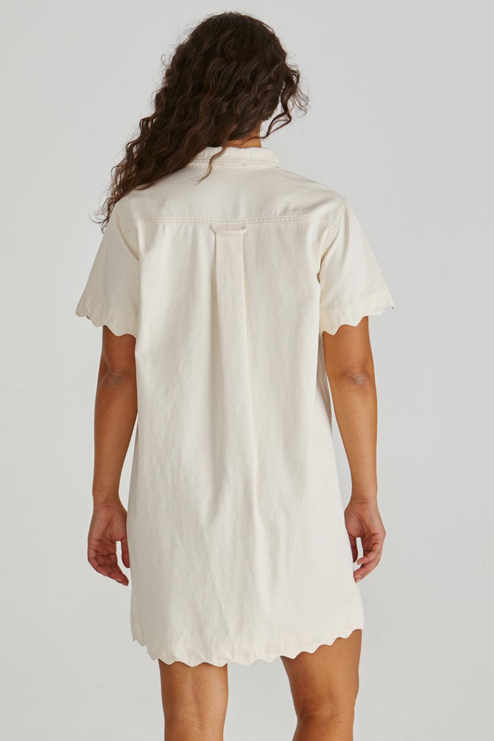 A model wearing the Vale Scalloped Denim Dress in colour Parchment (White), from the back