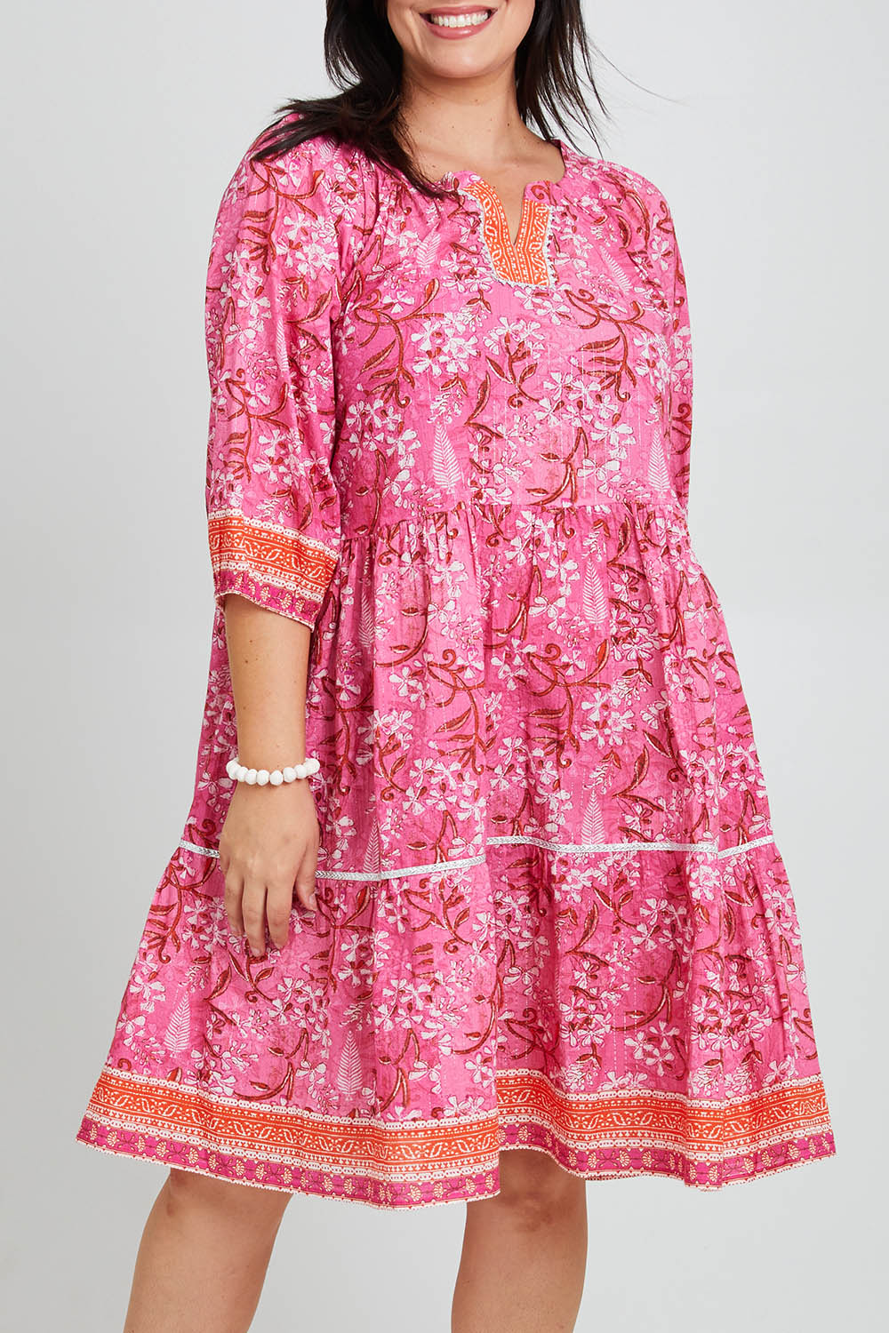 Model Poppy wearing size 16 of the Sandy Bay Dress in colour Pinkorange (Pink), from the front, cropped image