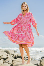 Model Riina wearing size 10 of the Sandy Bay Dress in colour Pinkorange (Pink), from the front, showing the whole outfit