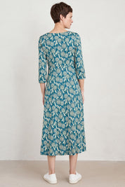A model wearing the Three Quarter Secret Cove Dress in colour Dandelion (Blue), from the back