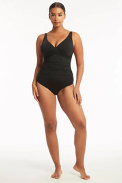 A model wearing the Eco Essentials Cross Front One Piece in colour Black (Black), from the front, showing the whole outfit