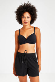 Model Olivia wearing size S of the Mid Length Boardshort in colour Black (Black), from the front, cropped image