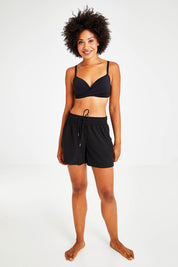 Model Olivia wearing size S of the Mid Length Boardshort in colour Black (Black), from the front, showing the whole outfit