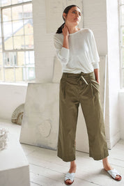 A model wearing the Maddelena Trousers in colour Desert (Green), from the front, showing the whole outfit