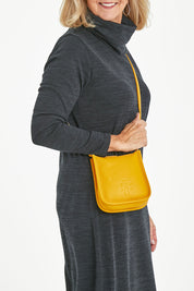 Model Sandy wearing size OneSize of the Small Leather Crossbody Bag in colour Mustard, from the front, cropped image